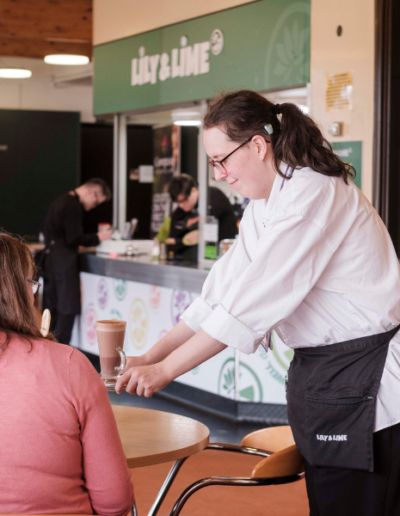 Waitress serving a hot chocolate to a customer sitting down at a table.