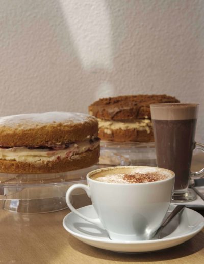 Cup of coffee and a tall glass of hot chocolate in front of two homemade cakes