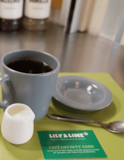 Cup of Americano and small jug of milk next to a Lily and Lime cafe loyalty card.